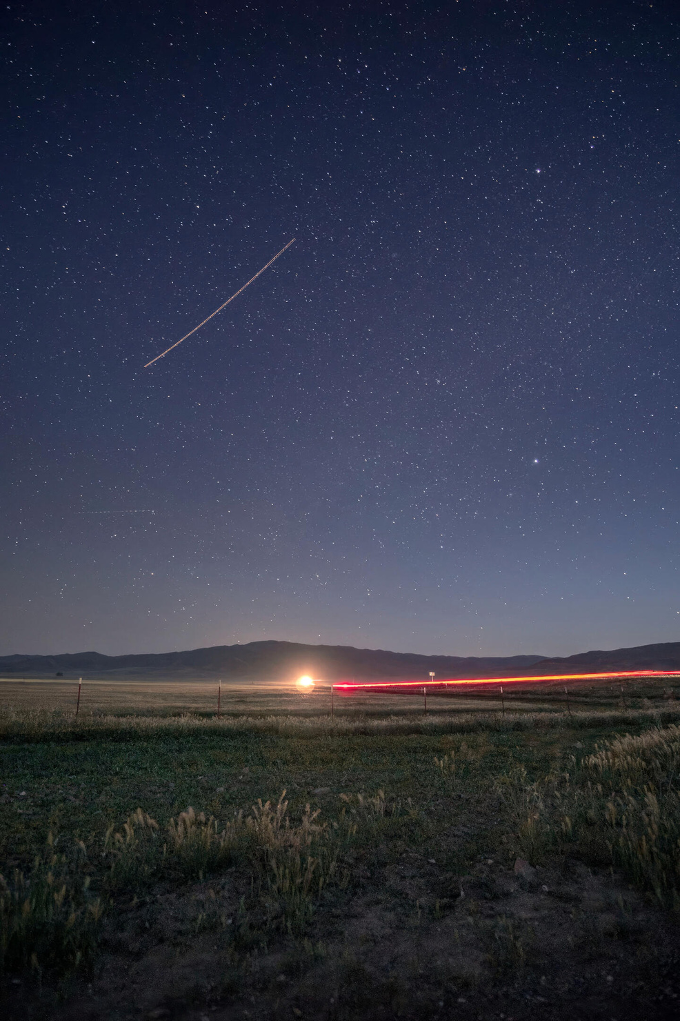 Long exposure night sky image on highway 41 in California. An airplane streaks through the sky, as well as the red of a car's taillights