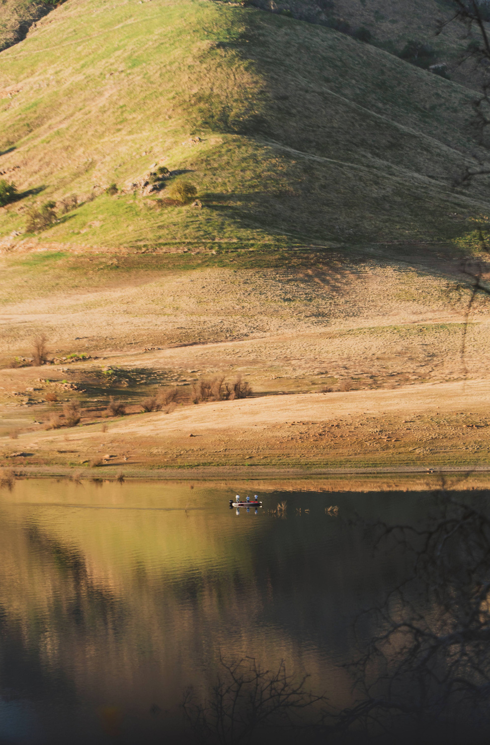 The Fishermen Fisherman on small boat at Lake Kaweah, backed by a scenic green and yellow mountain.
