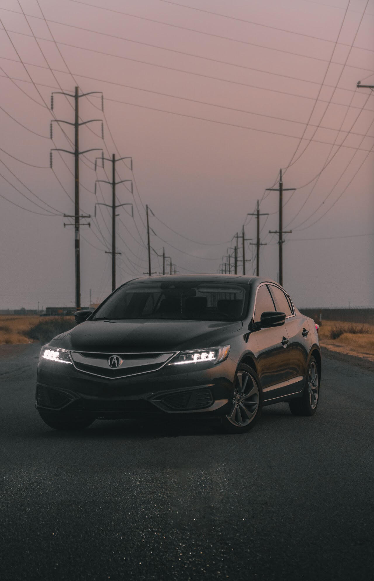 Acura ILX A black Acura on an empty road with vibrant yellow grass growing alongside