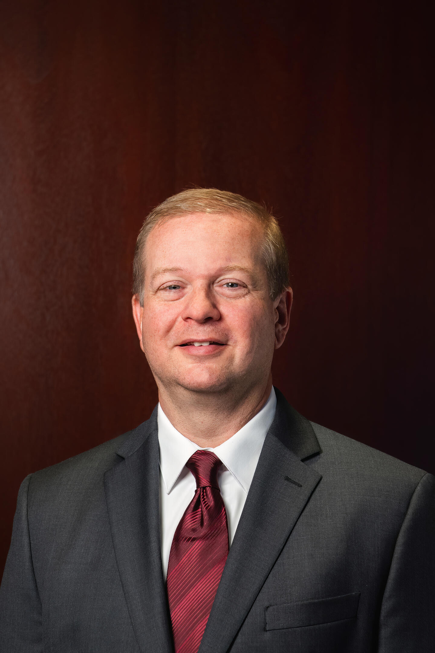 A lawyer stands against a dark wood background, exuding professionalism. He wears a crisp suit with a vibrant red tie, symbolizing power and authority