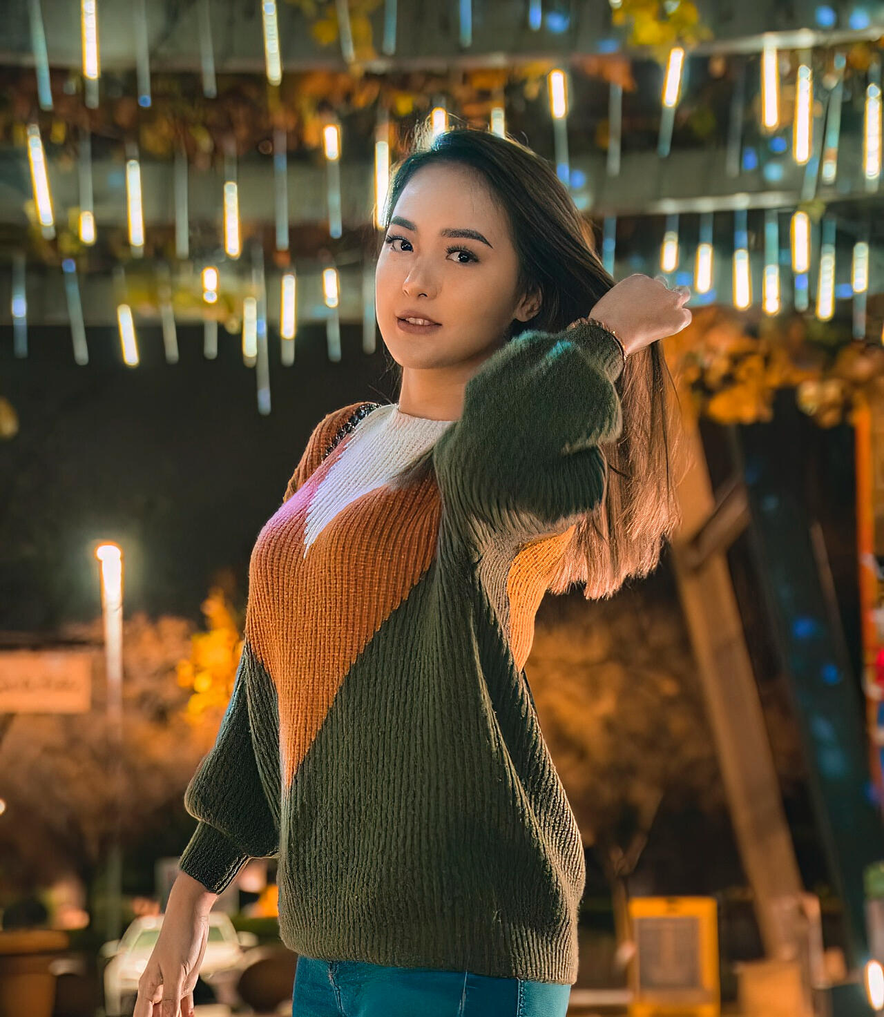 A Woven Sweater An enchanting evening portrait of a young woman in a cozy woven sweater, gazing into the camera amidst the shimmering backdrop of decorative lights