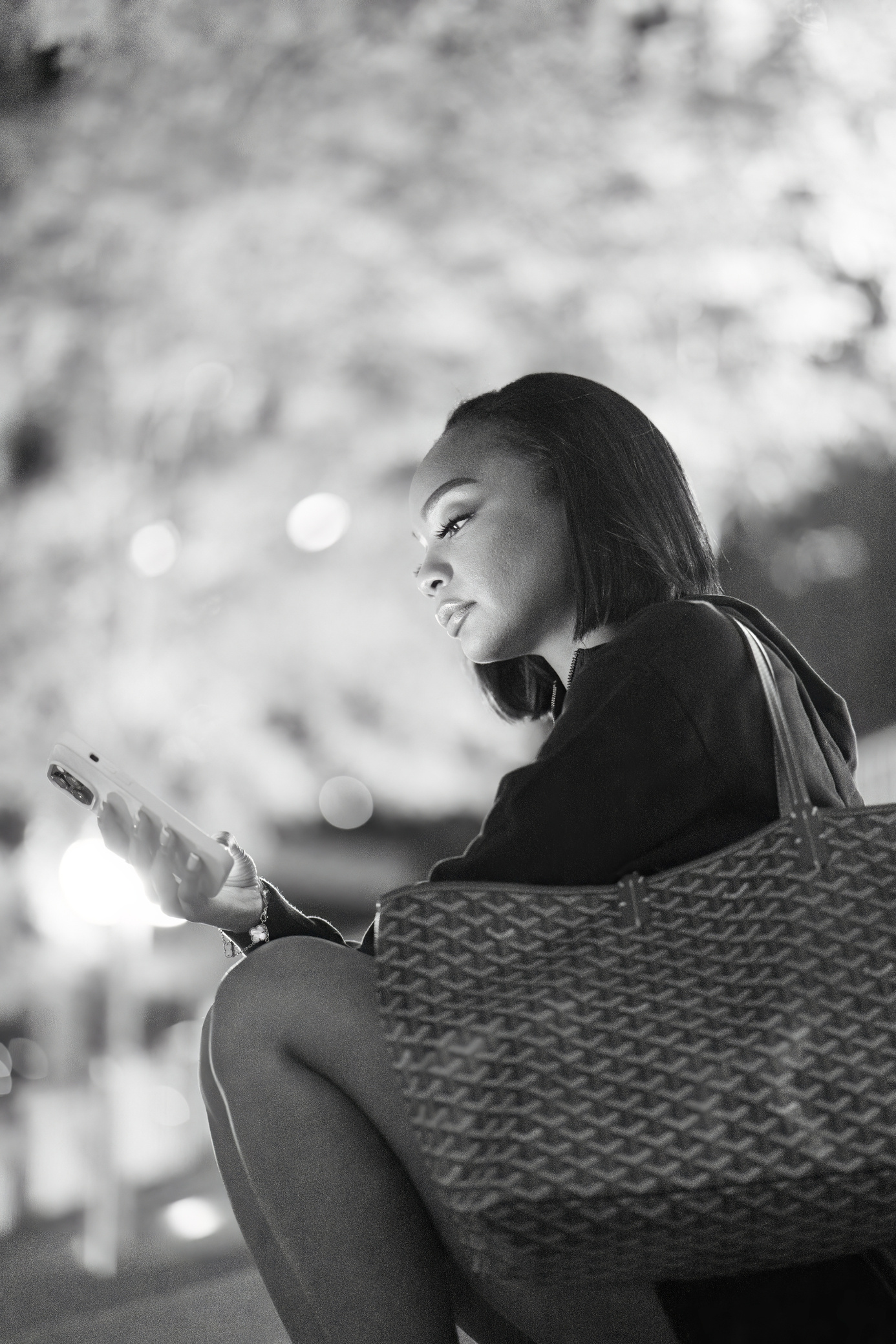 A young woman sits on the stairs at Chicago's Riverwalk with a bag beside her, scrolling on her phone.