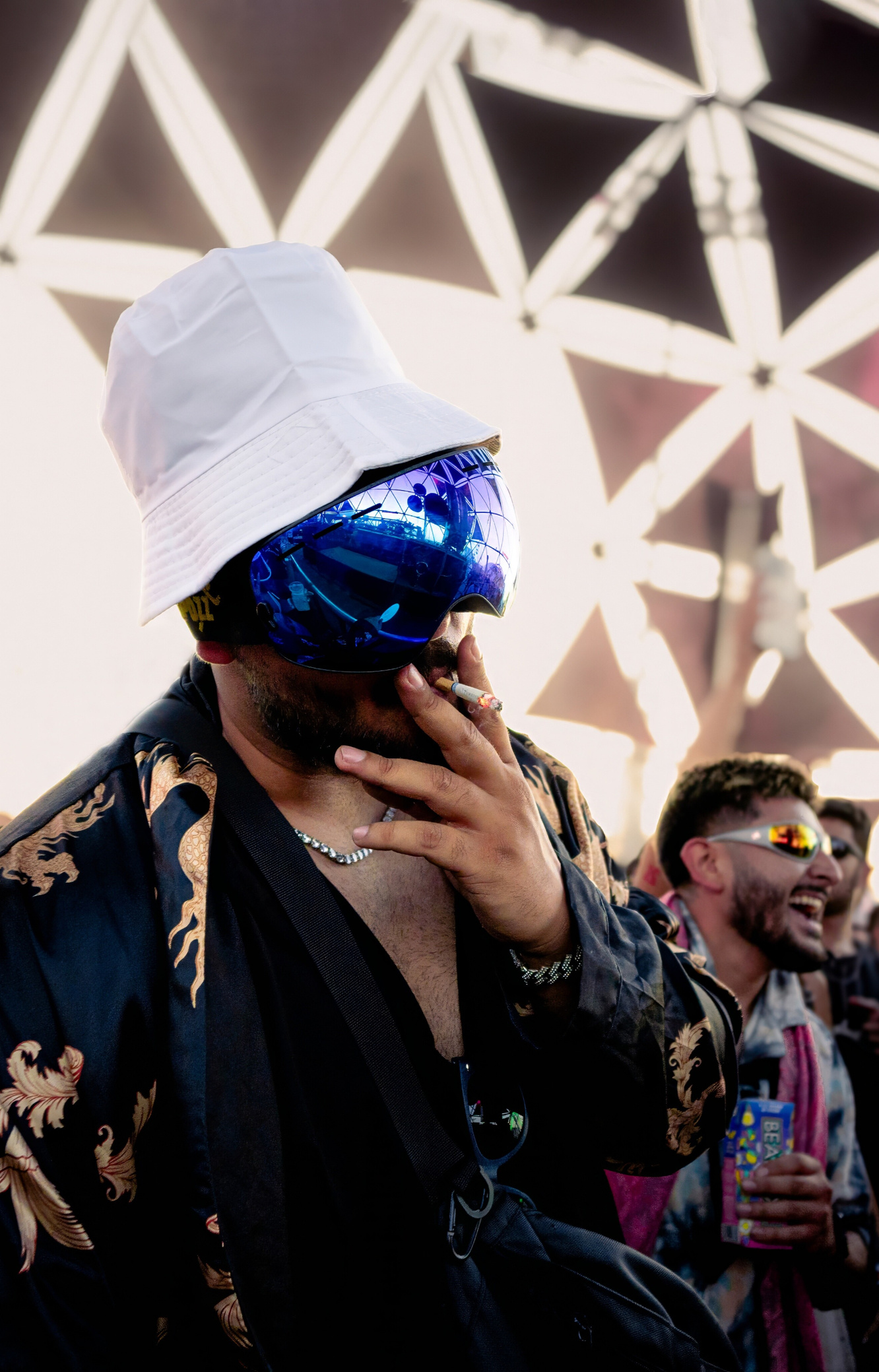 Festival Vibes Man wearing purple ski goggles and a white bucket hat smoking a cigarette at an EDM festival.