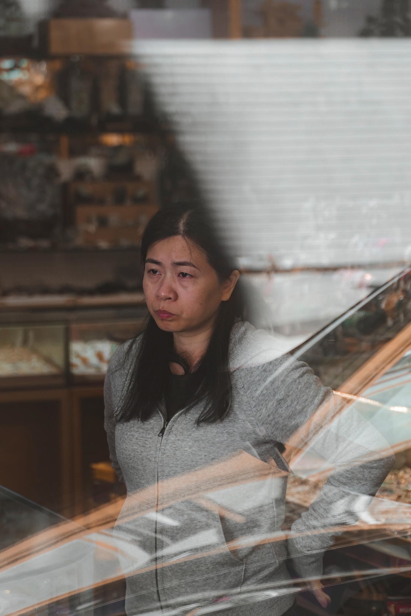 The Shop Owner An image of an Asian female shop owner looking out the window of her jewelry store with reflections of the street visible